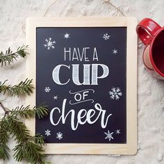 a chalkboard with the words have a cup of cheer written on it next to a mug