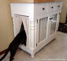 a black cat hiding in a white cabinet with curtains on it's sides and the door open