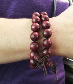 12mm Violet Wood Purpleheart wood beads strung on elastic cord fits a 6.5 inch wrist.  2mm hole. As our mala are hand-carved and assembled from natural materials, bead and tassel appearance may vary.  The beads are 12mm wide.  $12 per bracelet (our model is wearing two bracelets in the photo). Violet Wood Purpleheart meaning: Purpleheart gets its name from the color of the wood.  Its scientific name is Peltogyne.  It has other names in addition to Violet Wood and Purpleheart, such as Amendim and Adjustable Wooden Beaded Bracelets For Meditation, Traditional Wood Bracelets With Round Beads, Traditional Wooden Bracelets With Round Beads, Adjustable Wooden Bracelet With 8mm Beads, Traditional Wooden Bracelet With Round Beads, Adjustable Wooden Beaded Bracelets With 8mm Beads, Adjustable Wooden Beaded Bracelet With 8mm Beads, Wooden Beads Rosary Bracelet For Meditation, Meditation Rosary Bracelet With Wooden Beads