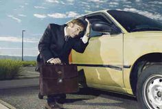 a man in a suit and tie holding a briefcase next to a parked yellow car