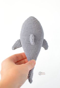 a hand holding a gray knitted stuffed animal in the shape of a whale with it's mouth open