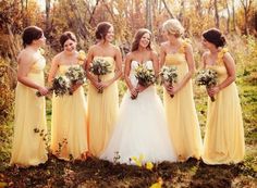 a group of women standing next to each other wearing yellow dresses and holding bouquets