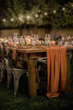 an outdoor dinner table set up with wine glasses and napkins on it, surrounded by string lights