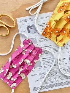 two face masks sitting on top of a table next to some scissors and sewing thread