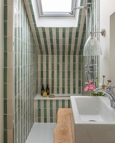 a small bathroom with green and white tiles on the walls, a skylight above the bathtub