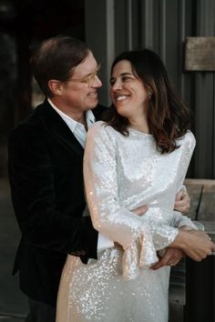 a man and woman standing next to each other in front of a metal structure with their arms around each other