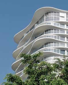 a tall white building with many balconies on it's sides and trees in the foreground