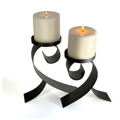 two white candles sitting next to each other on top of a metal holder with black ribbon