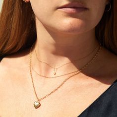 A woman with red hair and warm skin wears three gold chain necklaces. The choker has a tiny pearl charm and the longest necklace has a heart locket strung onto it. Elegant Heart Pendant Necklace With Figaro Chain, Elegant Yellow Gold Oval Link Charm Necklaces, Elegant Yellow Gold Oval Link Charm Necklace, Minimalist Yellow Gold Charm Necklace With Cable Chain, 14k Gold Cable Chain Charm Necklaces For Layering, 14k Gold Cable Chain Charm Necklace For Layering, Classic 14k Gold Charm Necklace With Cable Chain, Minimalist Yellow Gold Jewelry With Double Chain, Dainty Yellow Gold Link Charm Necklaces