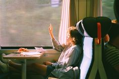 two people sitting on a train next to each other and one person raising their hand