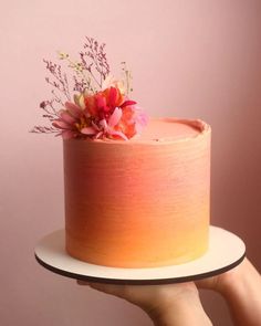 a person holding up a cake with flowers on top and frosting in the middle