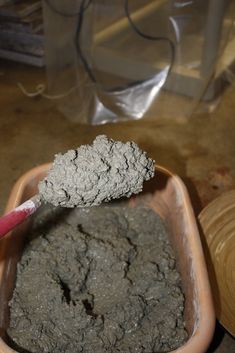 a spoon with some dirt in it sitting on a table next to a bowl filled with cement