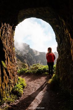 a woman in red jacket standing at the end of a tunnel with mountains in the background