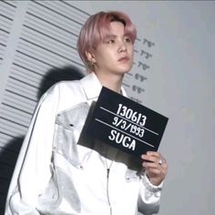 a woman with pink hair holding up a sign that says suga in front of her