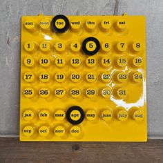 a yellow and black calendar sitting on top of a wooden table next to a wall