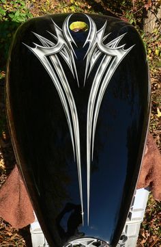 the front end of a black and white motorcycle parked next to a tree with leaves on it