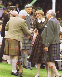 two women in kilts shaking hands with an older man