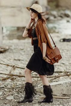 a woman in black dress and cowboy hat walking on the rocks with her handbag