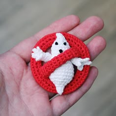 a hand holding a small crocheted ghost in a red circle with white hands