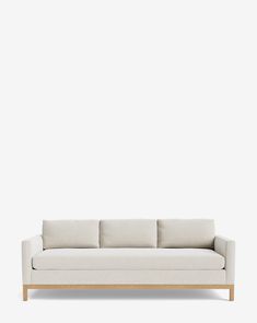 a white couch sitting on top of a wooden floor next to a wall with a light colored background