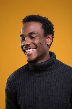 a man smiling and wearing a black turtle neck sweater with his eyes closed to the side