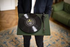 a man in a suit holding a record on a green tray with a black microphone