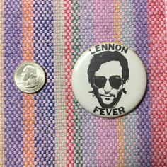 a button with the image of a man wearing sunglasses on it next to a penny