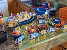 an assortment of snacks are displayed on a countertop in the kitchen, along with plates and bowls