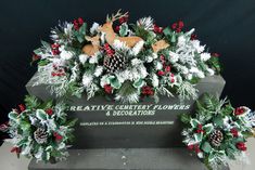 a christmas wreath with holly, pine cones and red berries on it sits in front of a grave