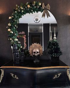 a black dresser topped with a mirror next to a christmas wreath and skull decoration on top