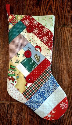 a christmas stocking made out of patchwork fabric on a wooden floor with red buttons