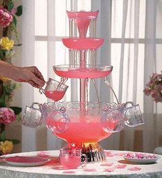 a woman is pouring pink liquid into a glass vase on top of a cake stand