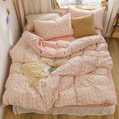 an unmade bed with pink and white comforter in front of a small window