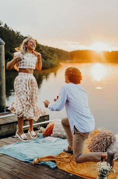 a man and woman dancing on a dock by the water at sunset, with one holding her leg up