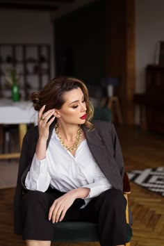 a woman sitting in a chair talking on her cell phone while wearing a white shirt and black pants