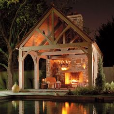 an outdoor fireplace and gazebo lit up at night next to a pool with water