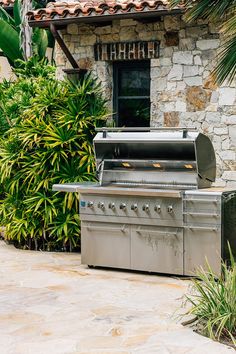 an outdoor bbq grill in front of a stone building with palm trees around it