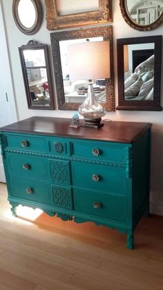 a blue dresser with mirrors on the wall above it and pictures hanging on the wall behind it