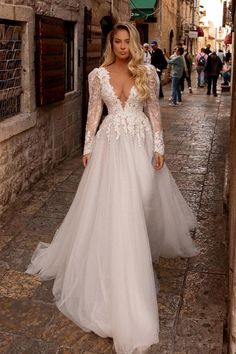 a woman is walking down the street wearing a wedding dress with long sleeves and an open back