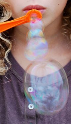 a young woman holding an orange toothbrush in her mouth and blowing bubbles out of it