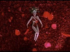 a woman floating in the air surrounded by red flowers and petals, with her head tilted to the side