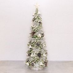 a small christmas tree with pine cones and white berries on the top is standing in front of a wall