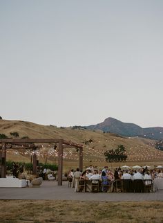 a group of people sitting at tables under umbrellas in the middle of an open field