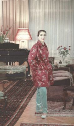 an old photo of a woman in a red kimono standing next to a piano