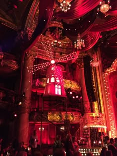 an elaborately decorated stage with red lights and chandeliers on the ceiling, surrounded by people