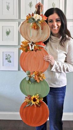 a woman standing next to a tall stack of pumpkins with flowers on it's sides