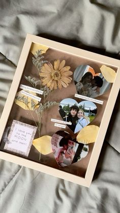 a shadow box with pictures and flowers in it sitting on a bed covered by gray sheets