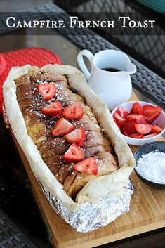 a french toast with strawberries on top and powdered sugar next to it, sitting on a wooden cutting board