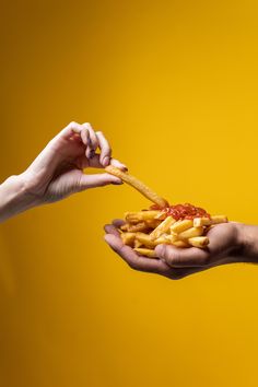 two people holding food in their hands against a yellow background with the other hand reaching for it