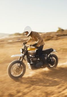 a man riding on the back of a white motorcycle down a dirt covered hill side